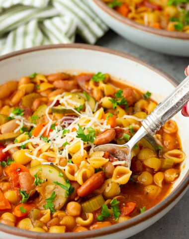 Minestrone soup in a bowl with a spoon and garnished with parmesan and parsley