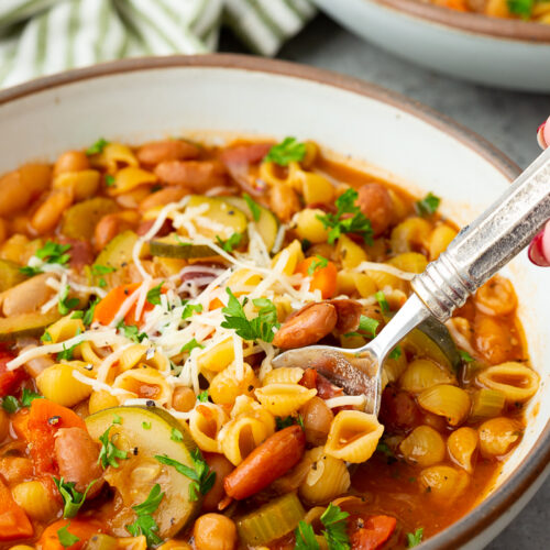 Minestrone soup in a bowl with a spoon and garnished with parmesan and parsley