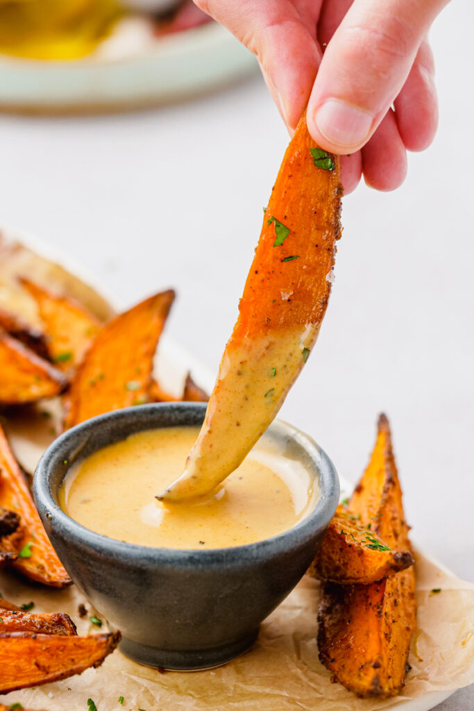 Roasted sweet potato wedge being dipped into a bowl of honey mustard sauce