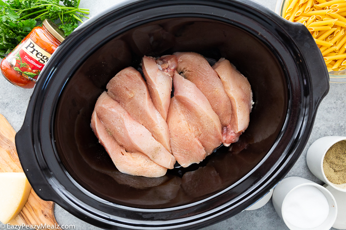 A slow cooker with raw chicken inside it. 