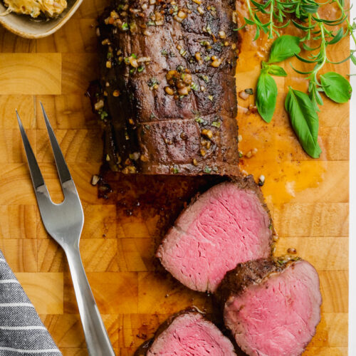 A half carved roast beef tenderloin on a cutting board