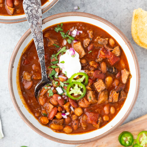 A bowl full of brisket chili, with various toppings and garnish around it.