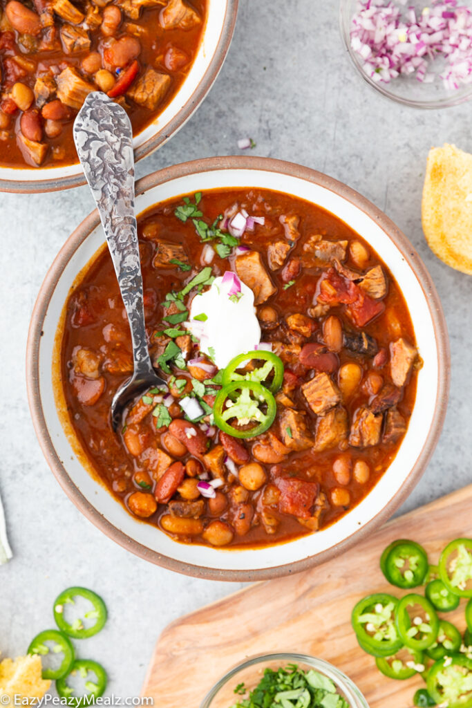 A bowl full of brisket chili, with various toppings and garnish around it. 