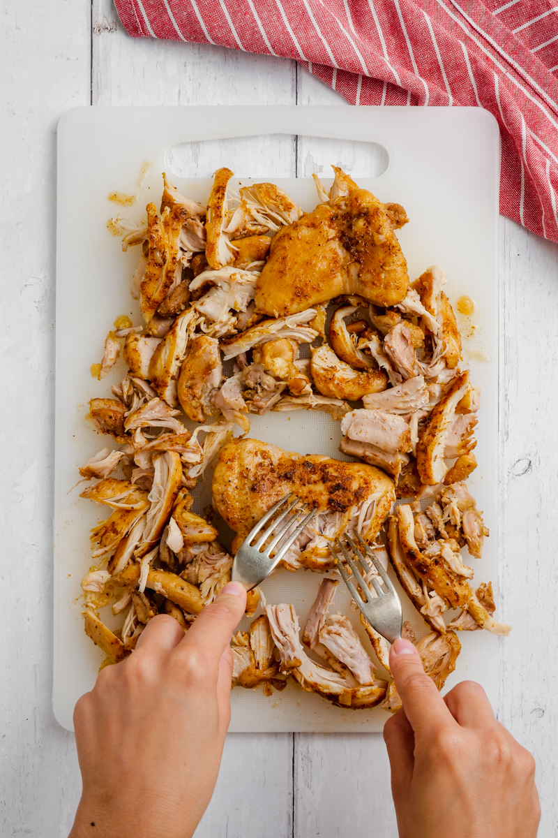 chicken thighs being separated by forks on cutting board