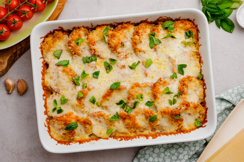 A white casserole dish filled with eggplant parmesan, garnish with basil