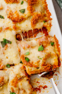 eggplant parmesan in white glass container on counter with spatula lifting out a square