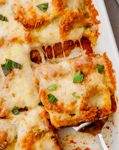 eggplant parmesan in white glass container on counter with spatula lifting out a square