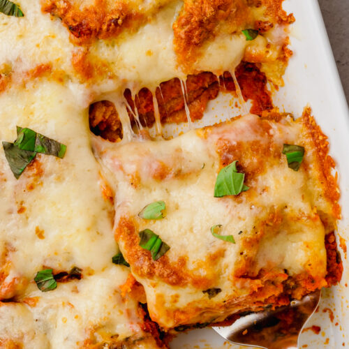 eggplant parmesan in white glass container on counter with spatula lifting out a square