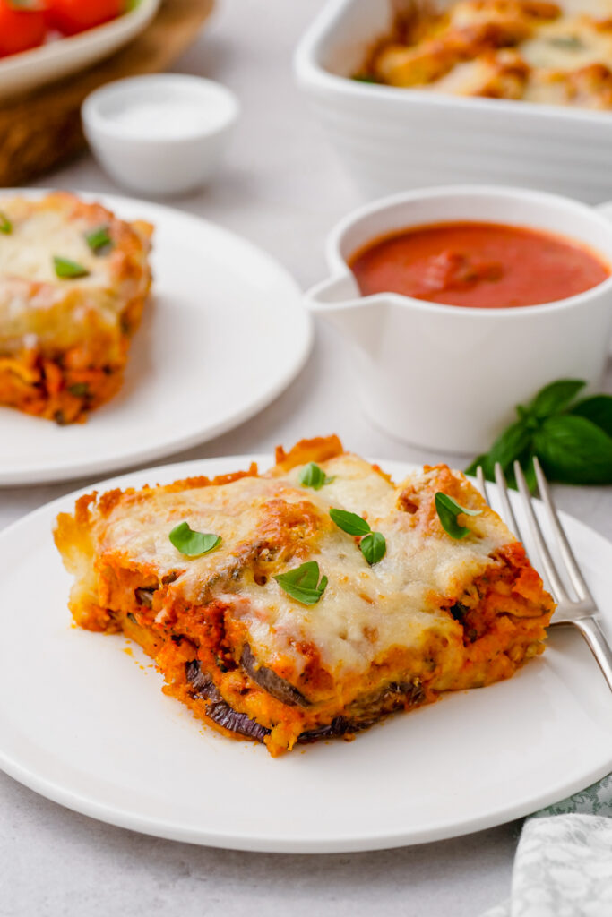 eggplant parmesan on white plate with fork to the side and sauce behind it.