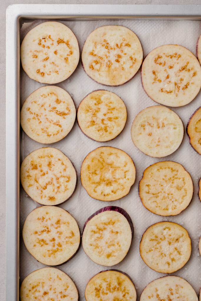 eggplant slices on pan under cooking sheet with salt on top.