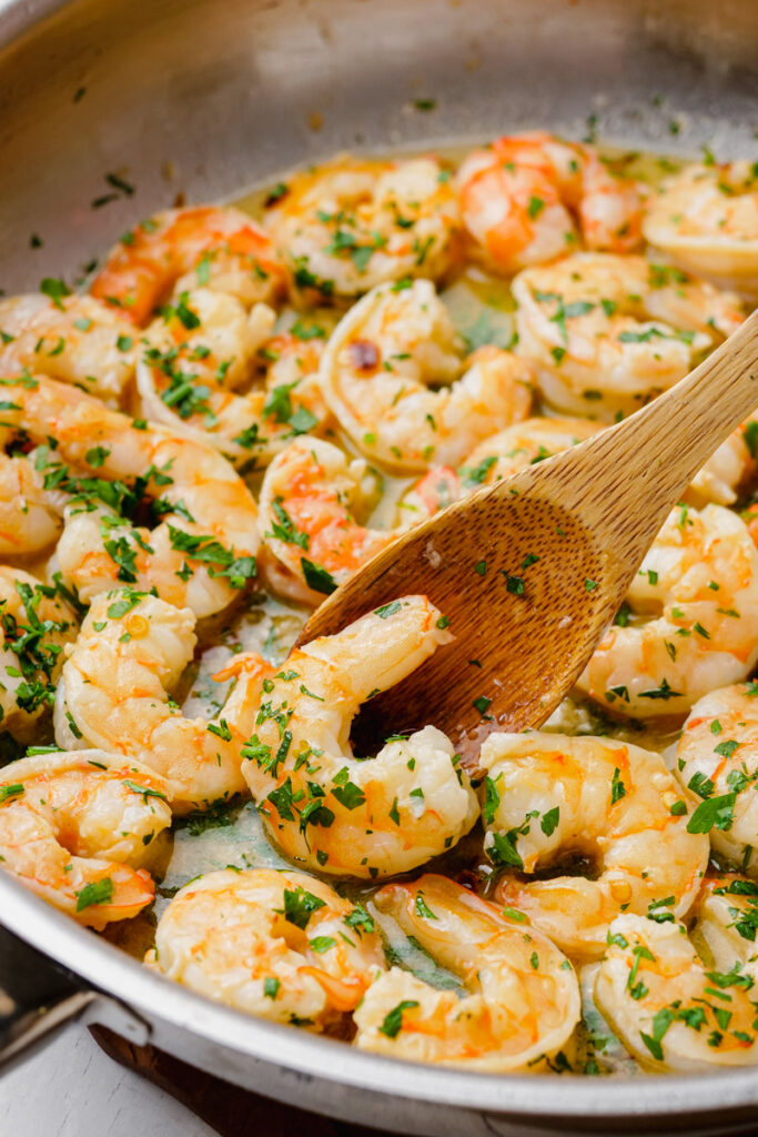 shrimp scampi being stored into the pot with wooden spoon