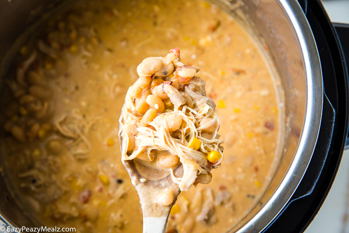 A spoon full of white chicken chili over a pressure cooker full of it. 