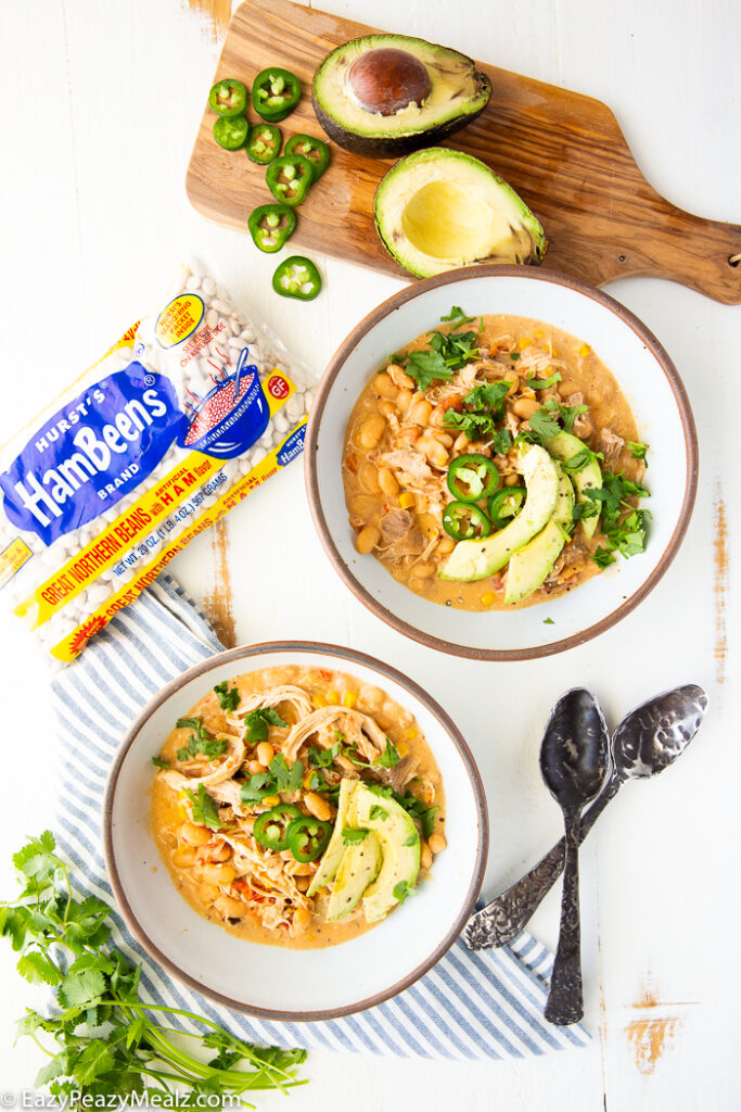 Two bowls of white chicken chili with garnish on top, and a bag of dry beans