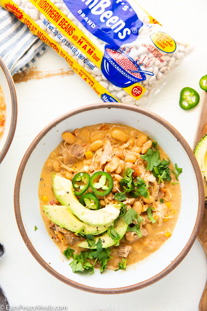 A bowl of white chicken chili topped with avocado, cilantro, and jalapeno. 
