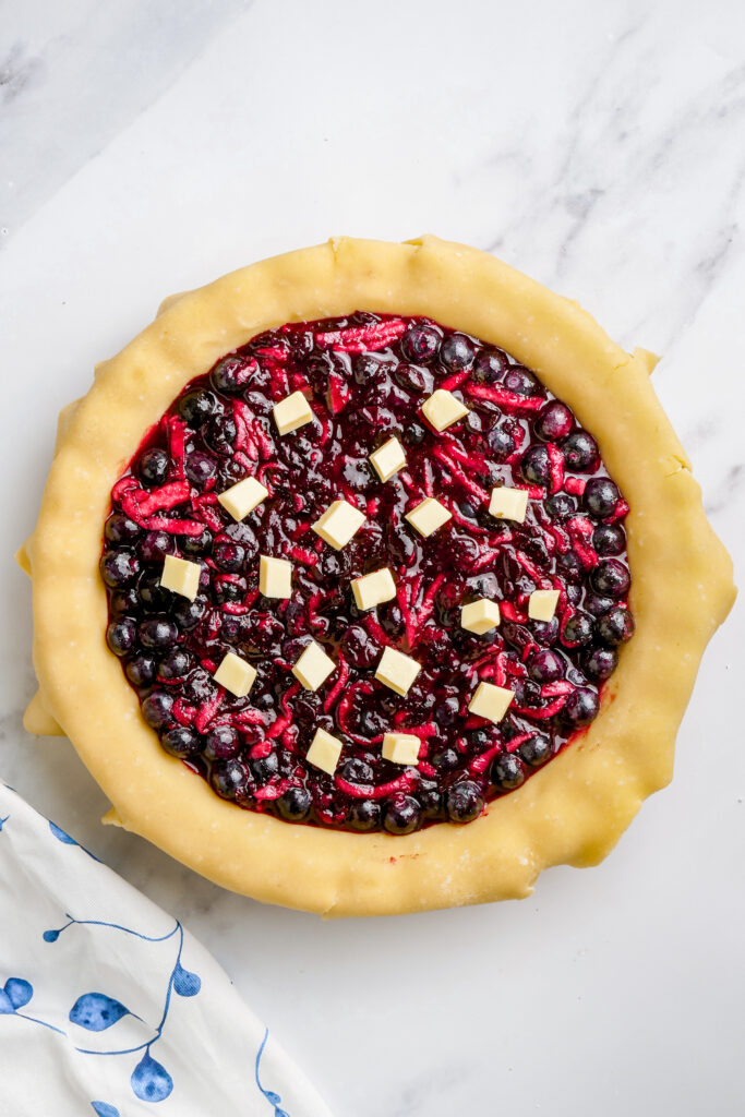 filling a pie with blueberry filling and dotting it with butter. 