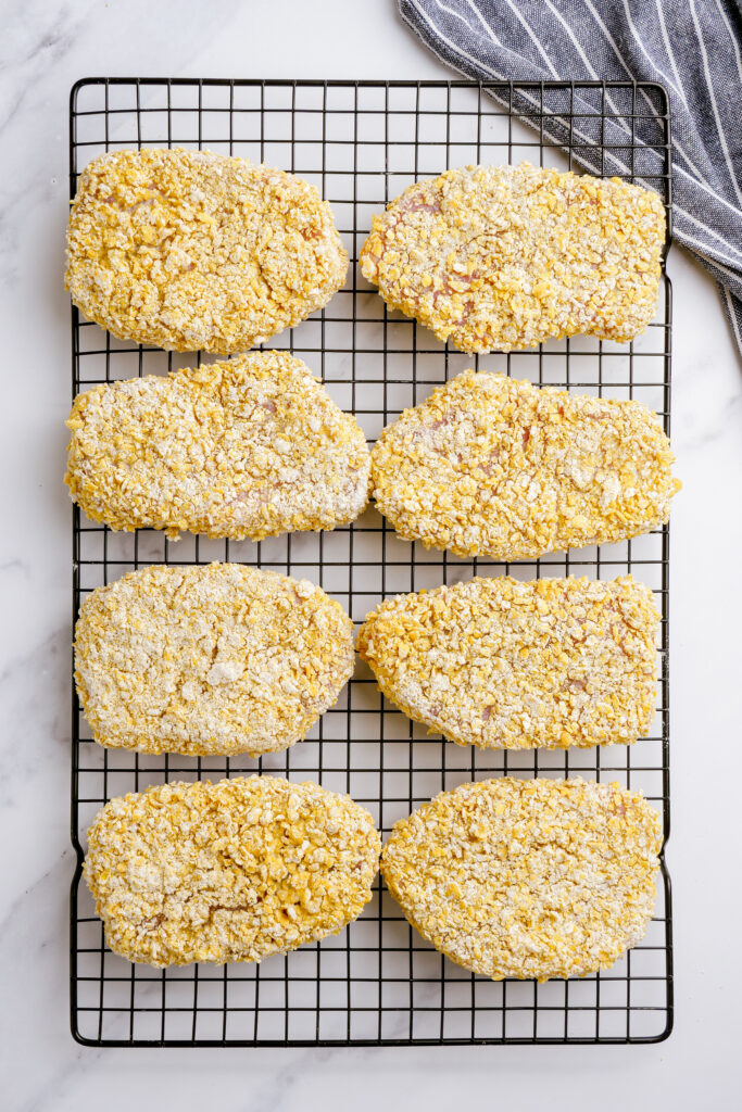 Breaded pork chops, ready to be cooked, sitting on a rack