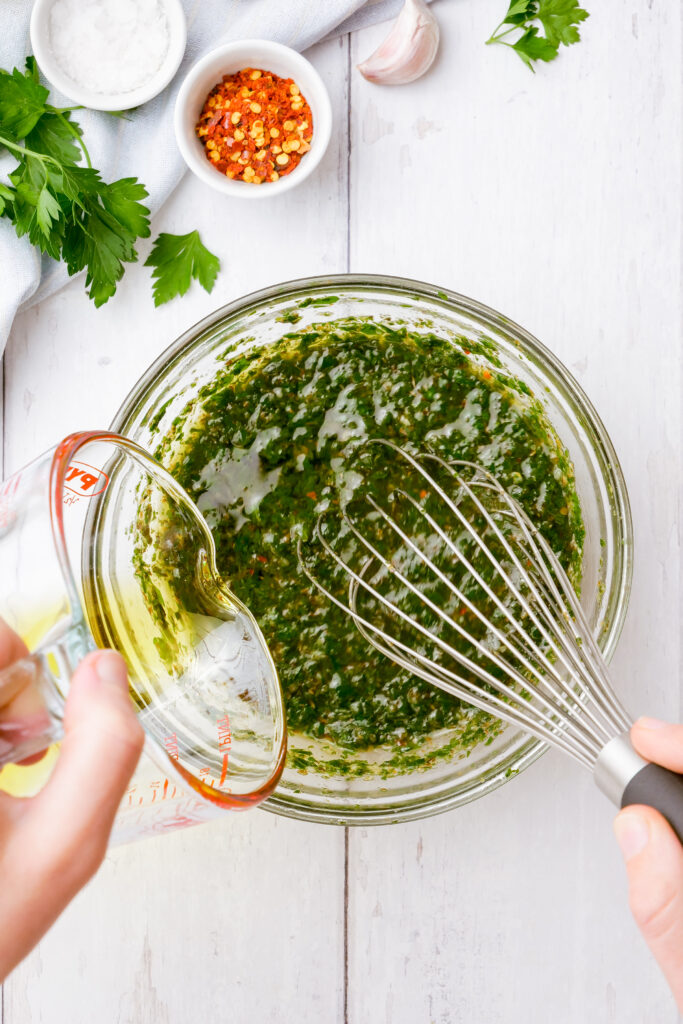 Whisking olive oil into chimichurri sauce until it emulsifies.