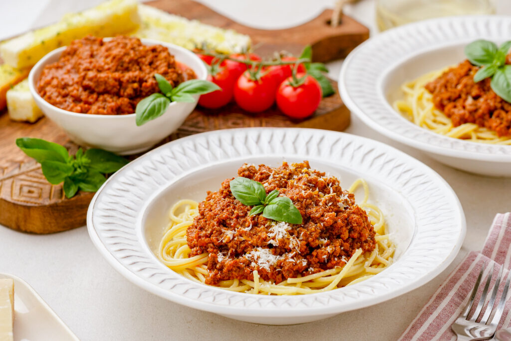 Slow cooker bolognese in a white bowl, served over pasta