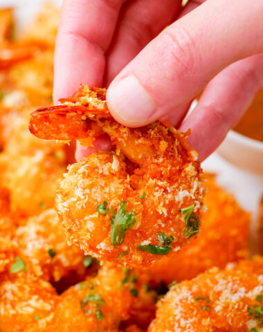 A hand holding a crispy oven baked shrimp, tail on