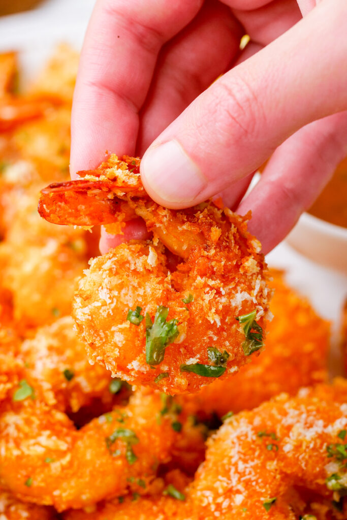 A hand holding a crispy oven baked shrimp, tail on