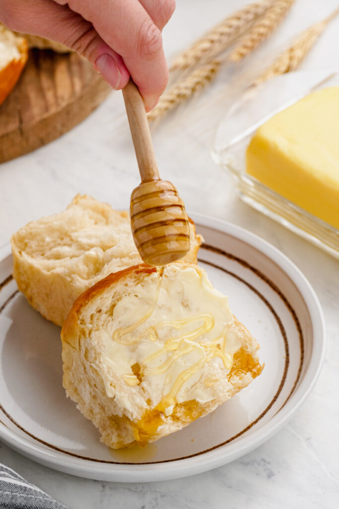 Dinner roll with honey being spread on it.