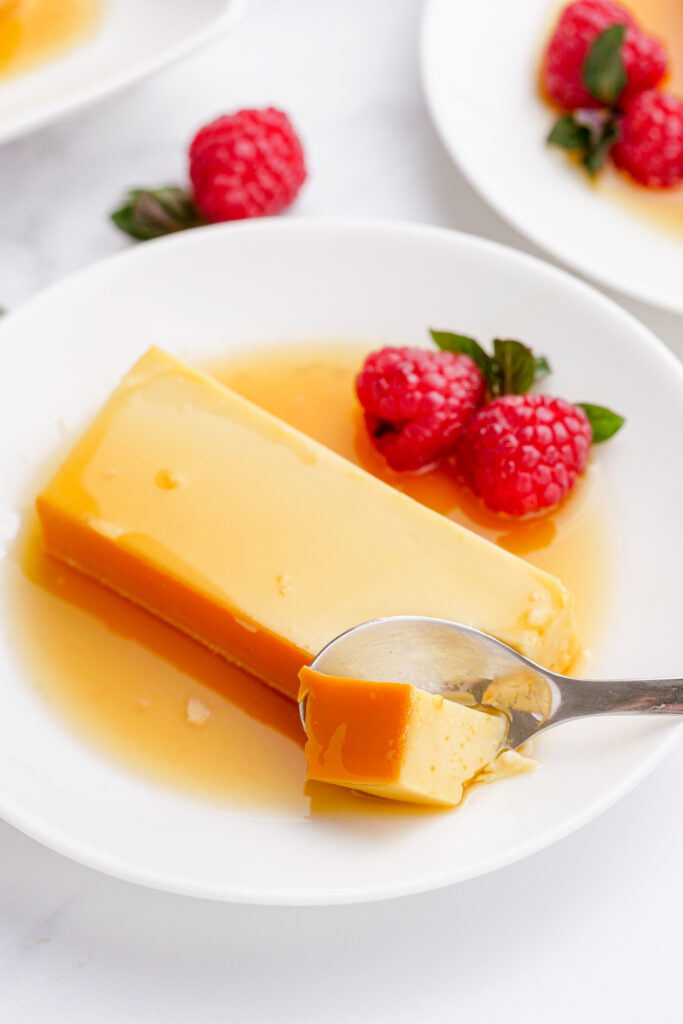 A plate of flan, with raspberries on the side. 