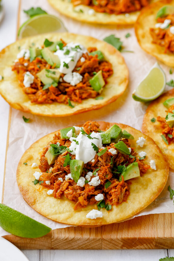 Tinga tostadas on a cutting board with lime garnishes