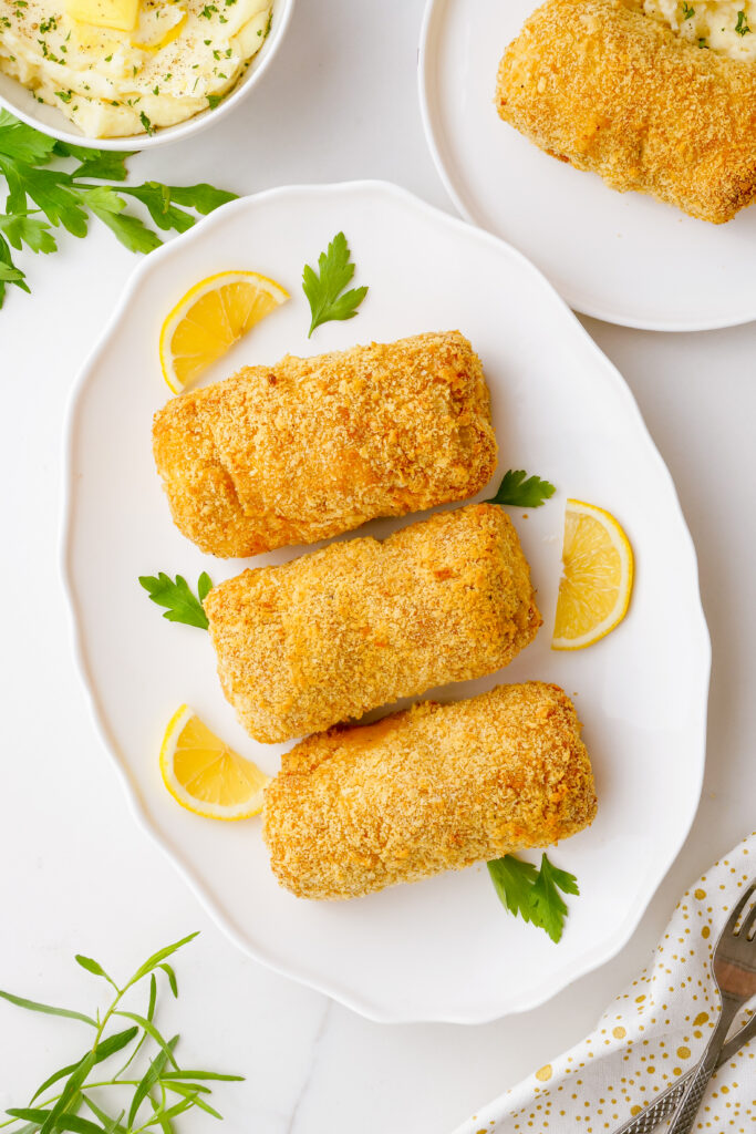 baked chicken kiev, a delicious baked chicken kiev on a white platter with lemons and herbs