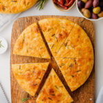 A loaf of homemade focaccia on a wooden cutting board.
