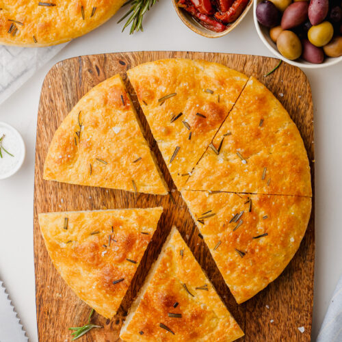 A loaf of homemade focaccia on a wooden cutting board.