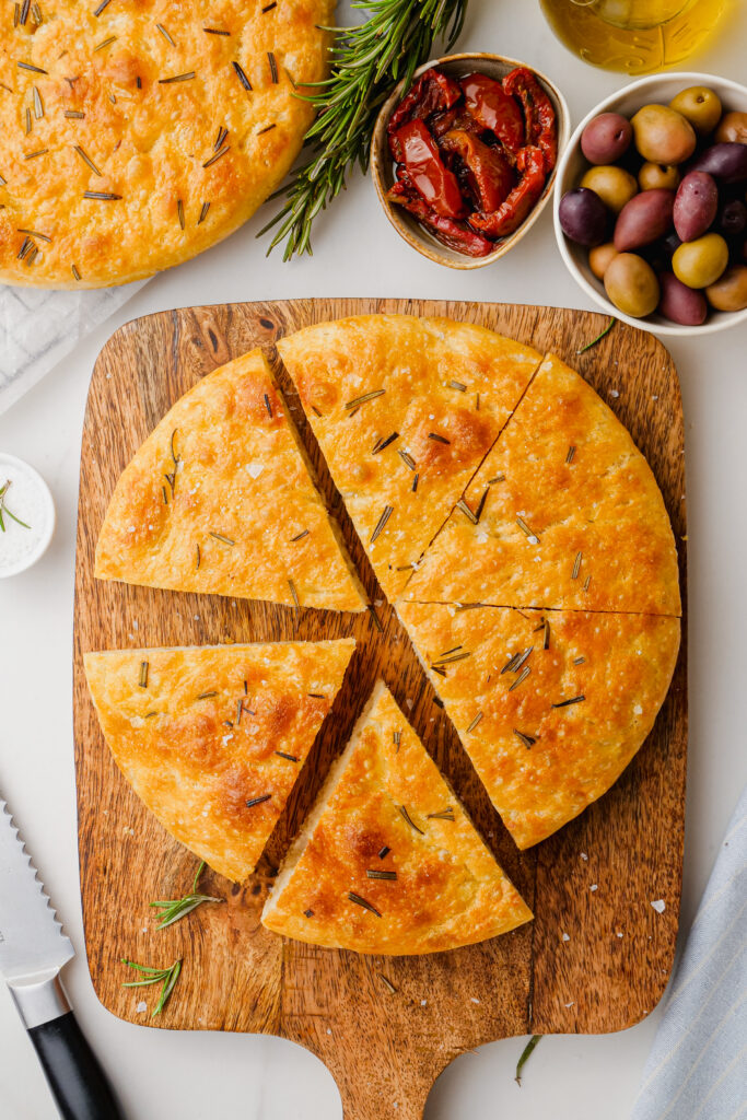 A loaf of homemade focaccia on a wooden cutting board. 