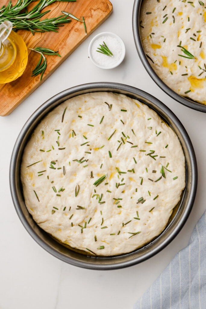 Sprinkled focaccia dough covered with rosemary and letting rest before baking