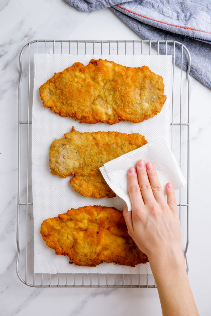 Blotting excess oil off the pork schnitzel with a paper towel