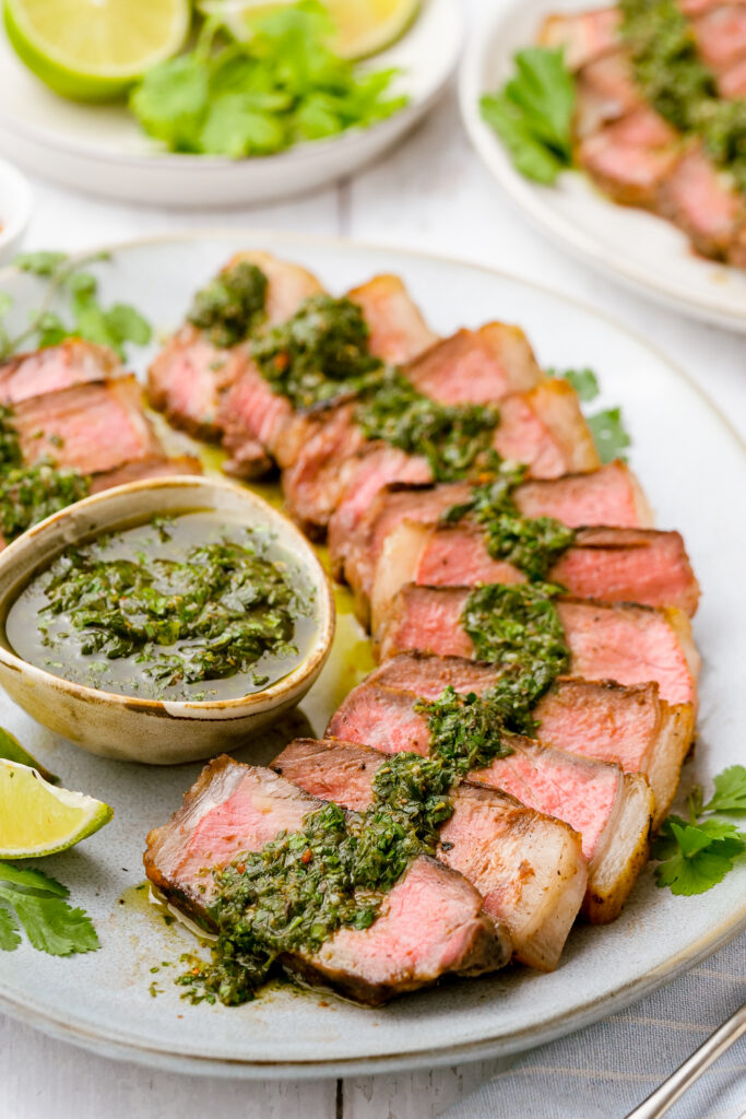 Steaks with chimichurri sauce, sliced and served on a platter. 