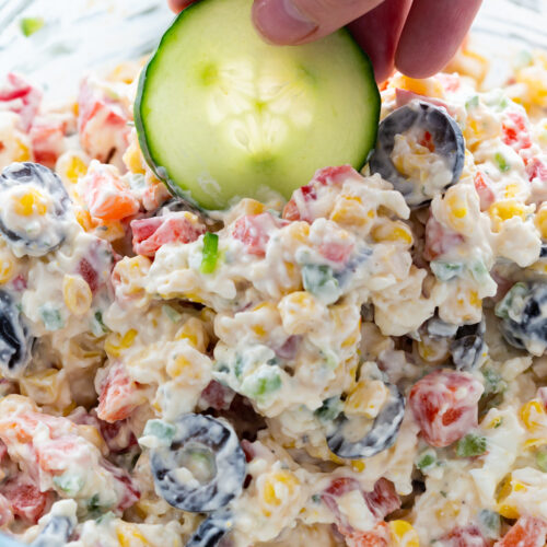 Loaded ranch dip with cucumbers being dipped into it.