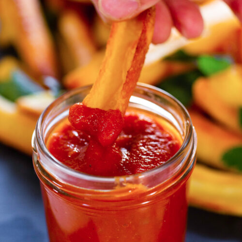 Homemade ketchup with fries being dipped into it.