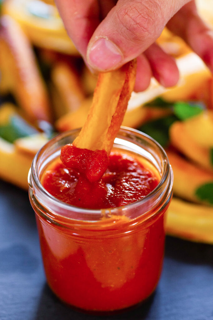 Homemade ketchup with fries being dipped into it.