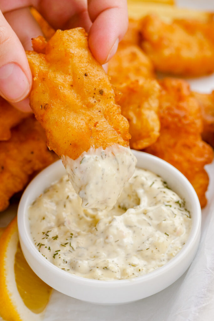 Fried fish being dipped in tartar sauce