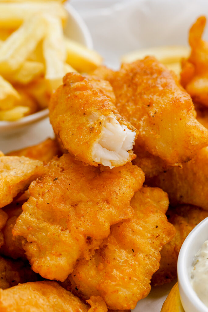 Beer Battered Fish:  crispy beer battered fish on a stack of other pieces of fish