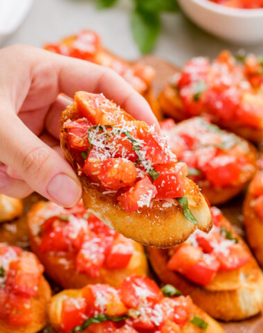 A bruschetta on crostini being held above a platter of bruschetta