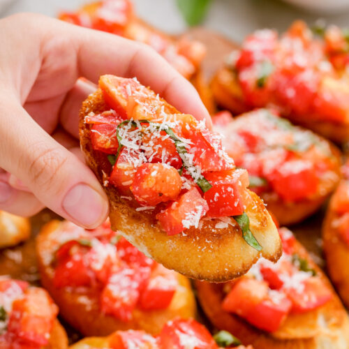 A bruschetta on crostini being held above a platter of bruschetta