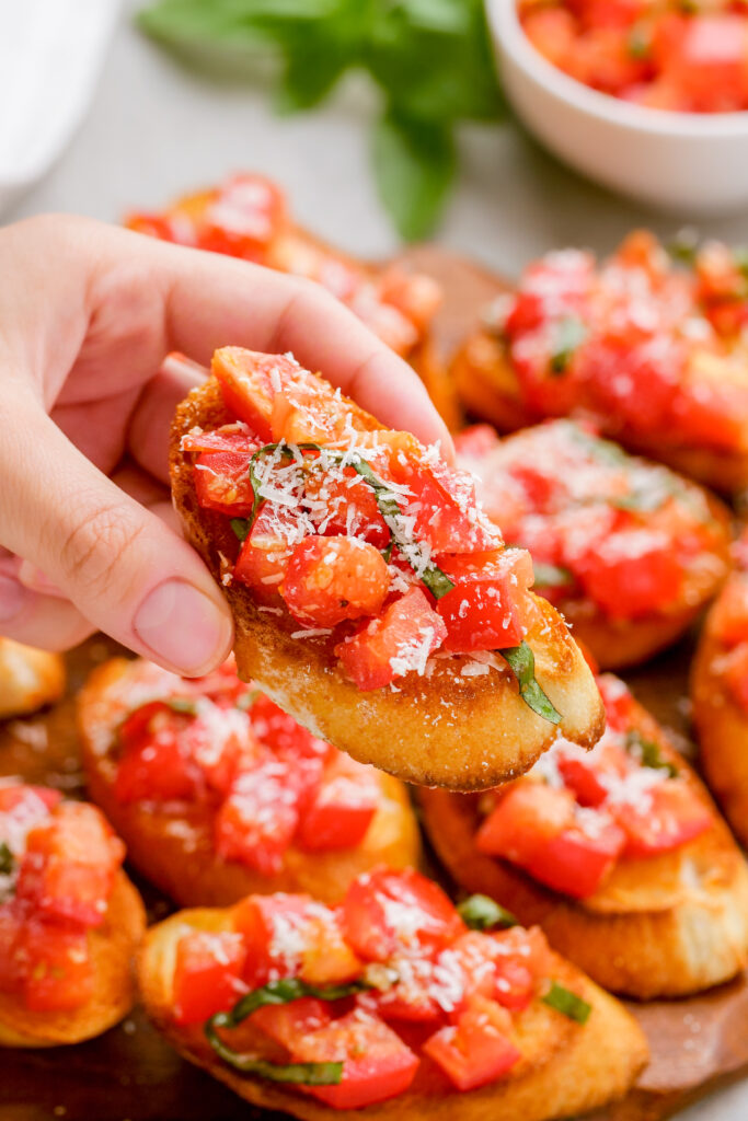 A bruschetta on crostini being held above a platter of bruschetta