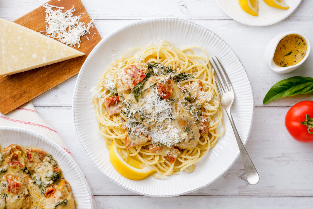 A plate of instant pot tuscan chicken over pasta with parmesan on top