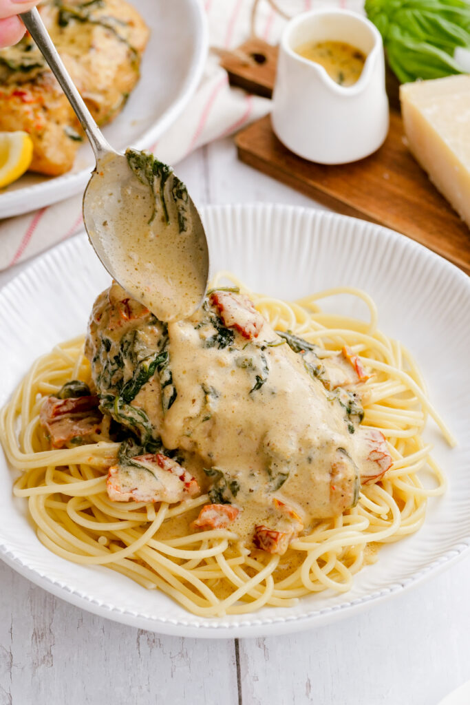 A piece of instant pot tuscan chicken with a spoon placing sauce over the top.