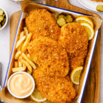 Oven fried chicken on a baking tray with sauce and fries