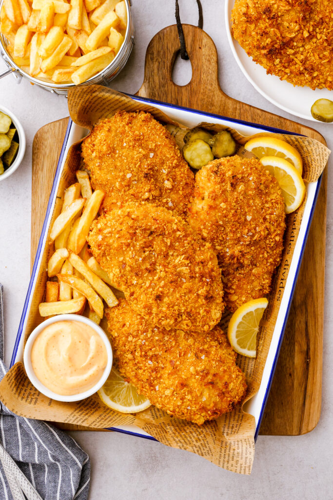 Oven fried chicken on a baking tray with sauce and fries