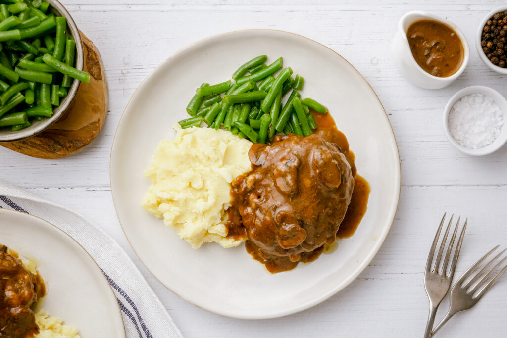 Salisbury steak and mashed potatoes and green beans on a white plate