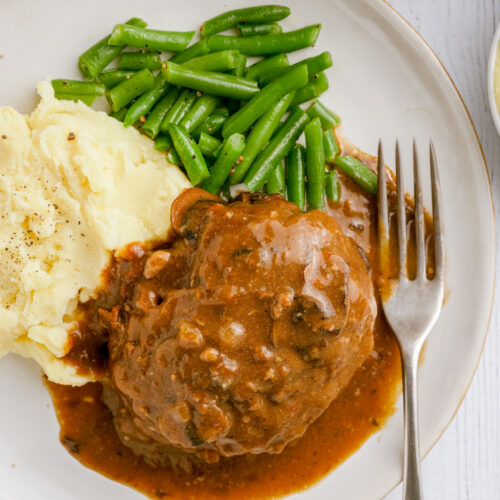 A white plate with salisbury steak, mashed potatoes, and green beans.