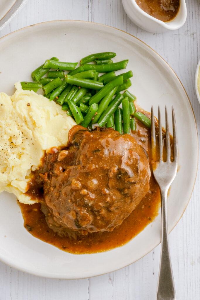 A white plate with salisbury steak, mashed potatoes, and green beans. 