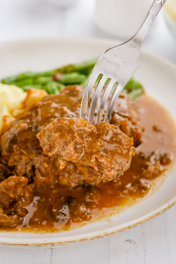 A plate of salisbury steak, the easiest most delicious recipe, with a fork full out of the patty